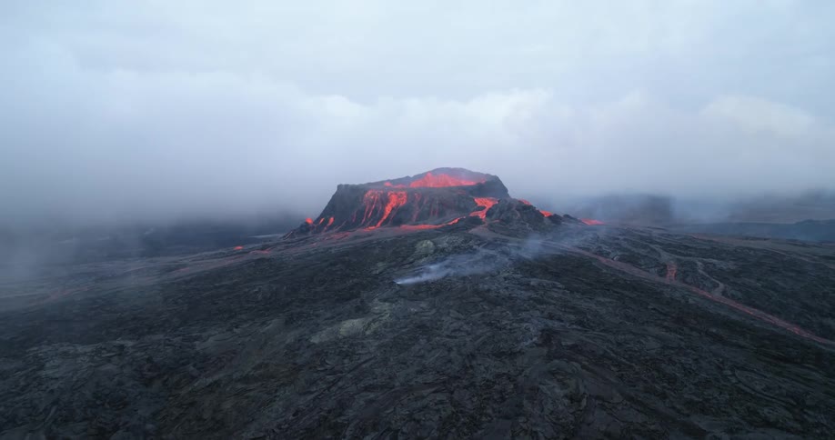 Smoke fills the air as orange lava glows in the top of a volcano
