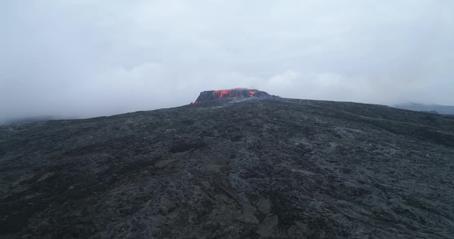 Molten lava erupts and flows down the side of a black volcano