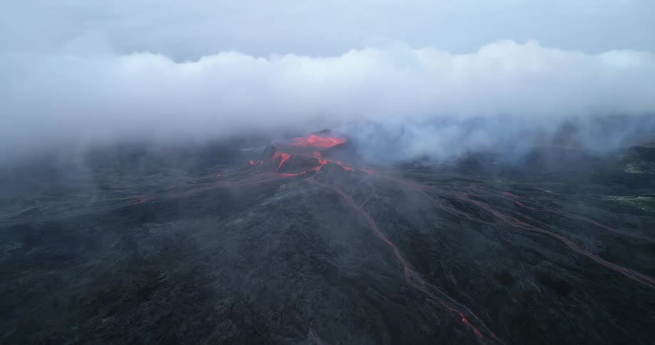 An aerial view of lava glowing and flowing from a volcano with dense smoke in the air during the daytime