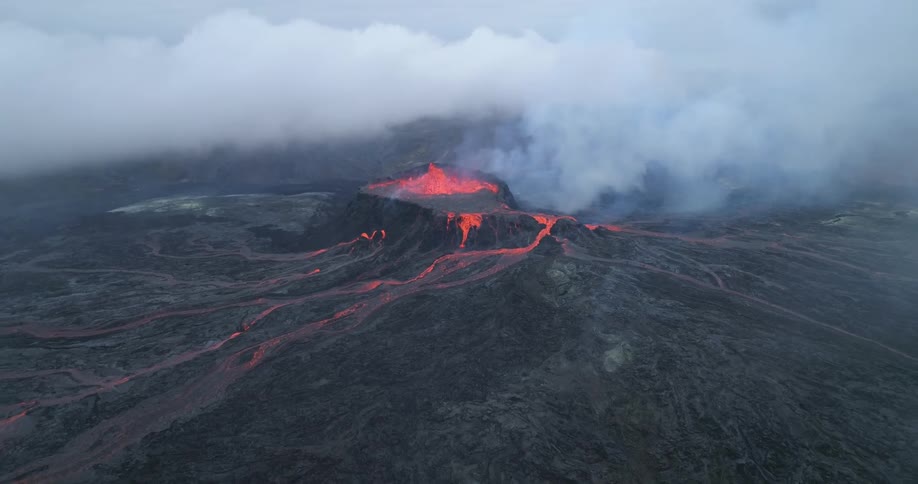 Smoke rises from erupting volcano as cloud bank flows across sky