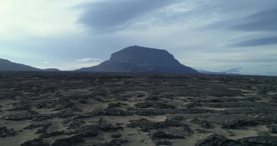 Dry ground and a mountain in the distance under a cloudy sky