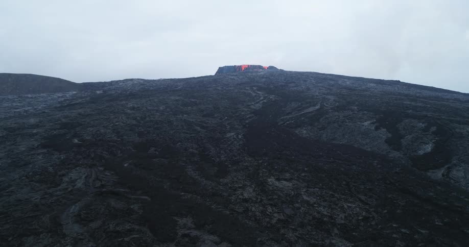Molten lava erupts and flows from a black volcano
