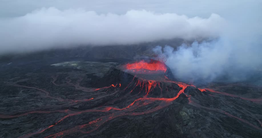 An aerial view of volcanic lava bubbling and flowing with smoke rising on a gray day