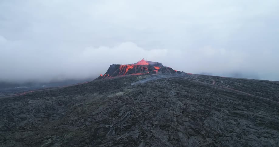 Bright orange lava bubbles and spills out the top of a volcano