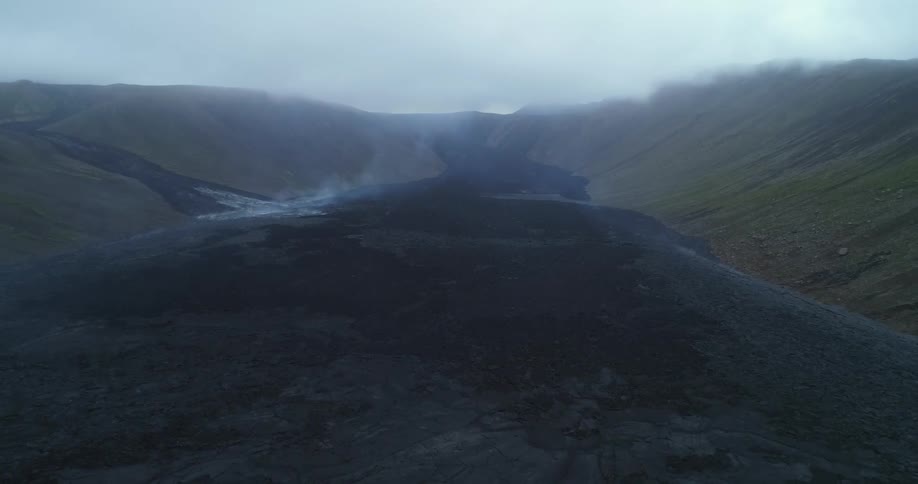 An aerial view of smoke rising from cooling lava flow from a volcano during the daytime
