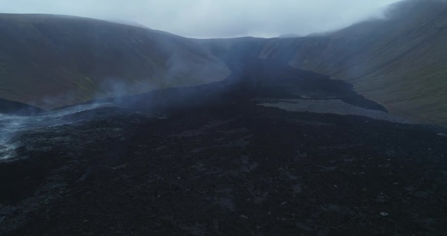 An aerial view of a volcano with cooling lava flow causing smoke to rise on a cloudy day