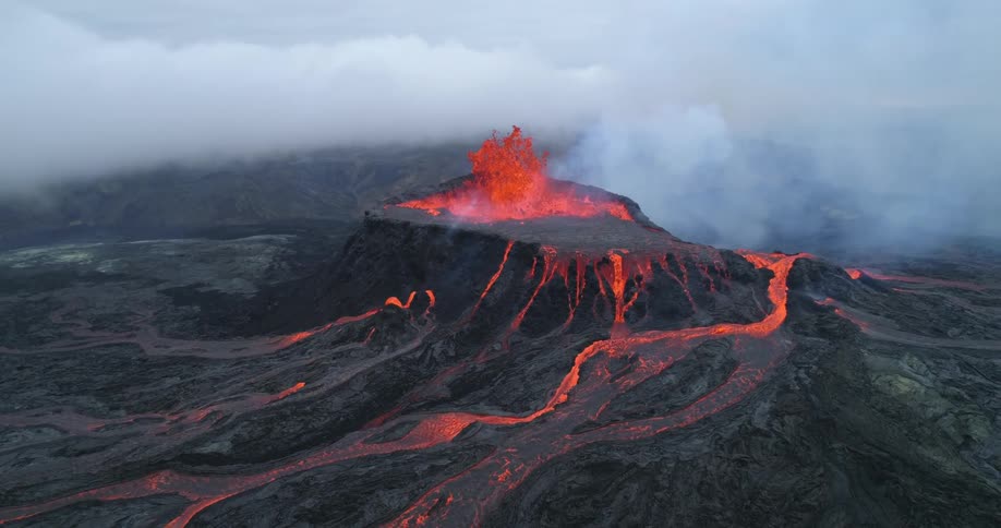 Lava is shooting out of and flowing down the side of a volcano