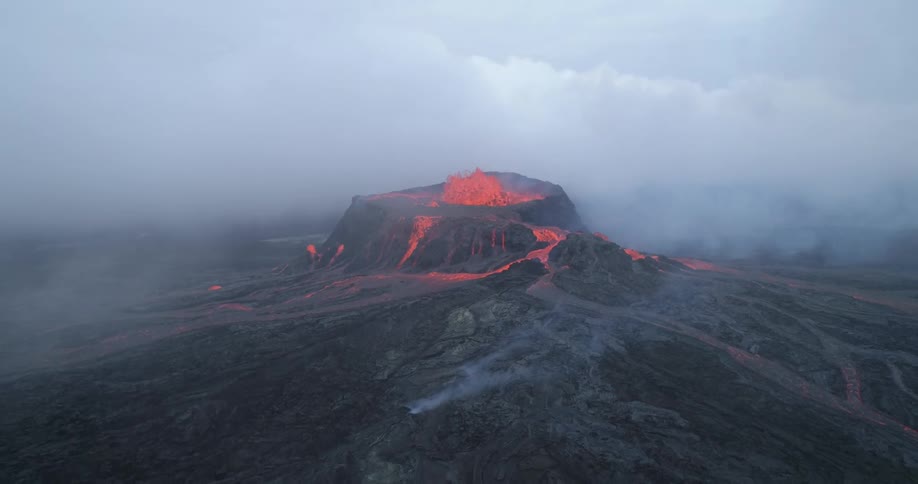 Lava bubbles up and flows over the sides of a black volcano as smoke and steam billow