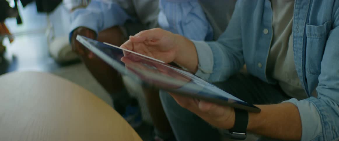 Two men in a room sitting by a table looking at a tablet with a wall in the background