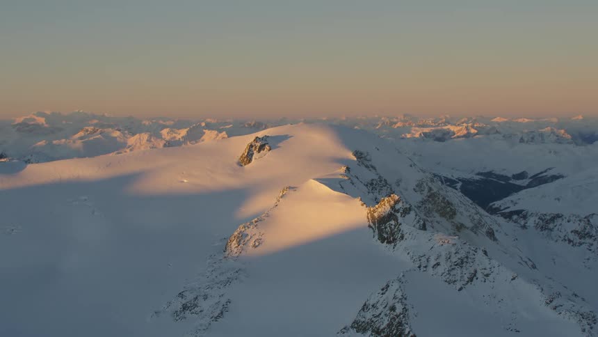 Sun touches peaks on snow covered mountains as rest of terrain remains in shadow