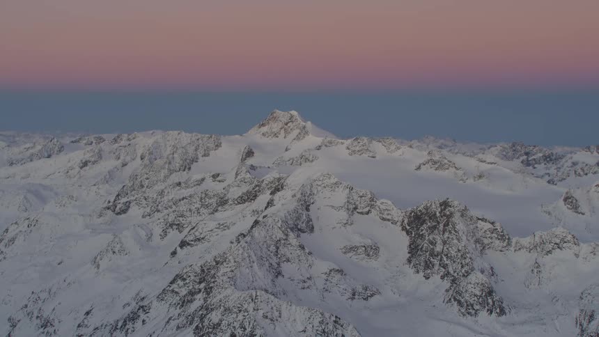 Snow covered mountain with a peak high in a pink and blue sky