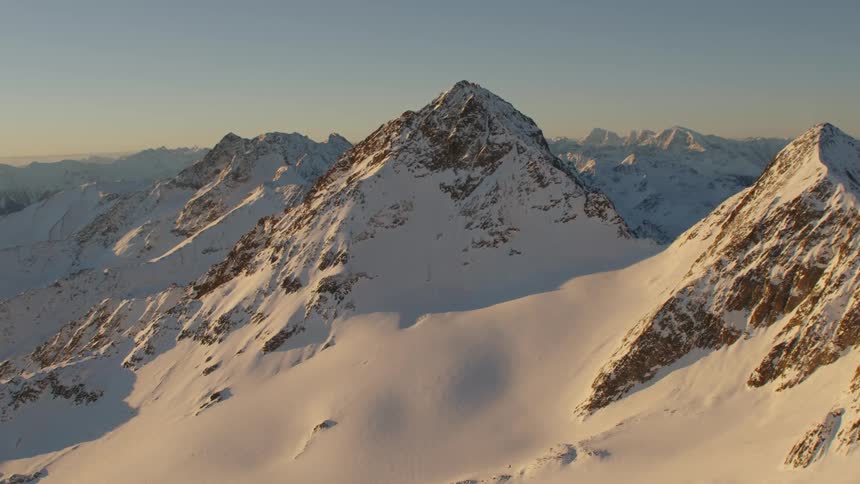 Morning sun is shining on the slopes of a vast mountain range partially covered in snow