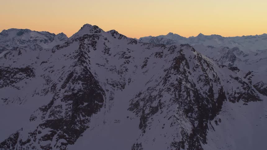 A mountain range of peaks partially covered in snow at sunrise