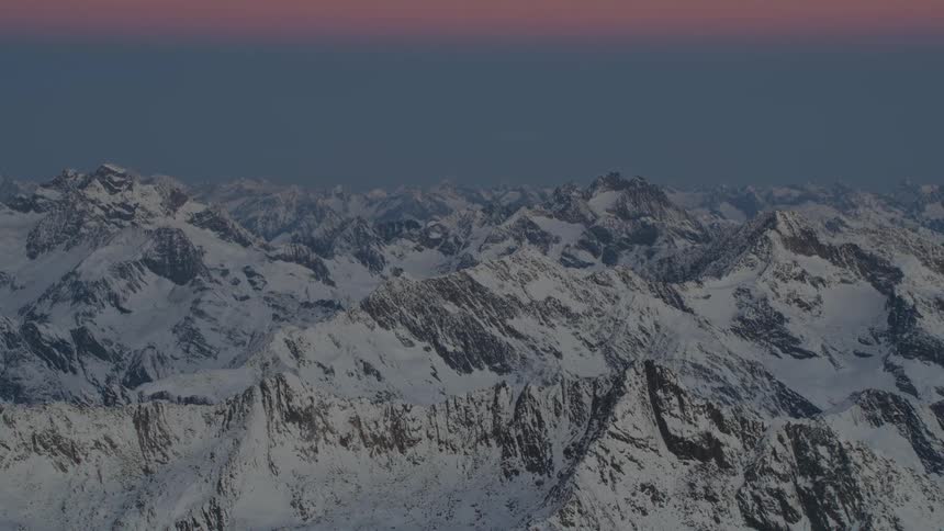 Snow covered mountains sit under hazy sky and red tinted clouds