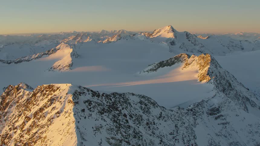 A mountain range covered in snow and ice with the sky and clouds in the background