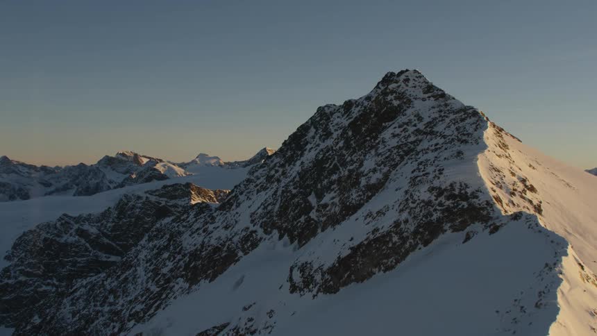 Sun brightens snowy mountain faces on one side of ridges leaving other slope and valley in shadow
