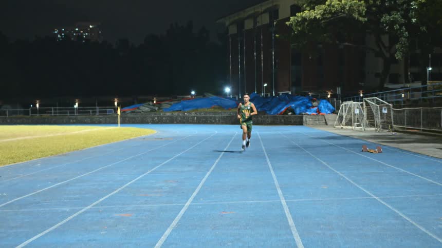 A teenage boy runs on a track outside a school