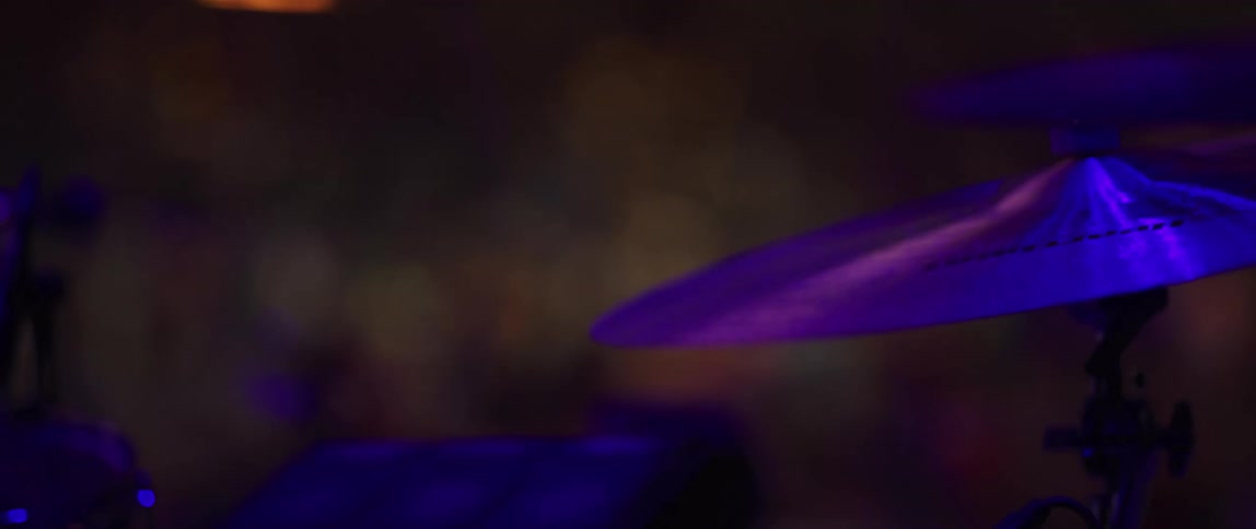 Cymbals vibrate as drummer strikes them under purple lighting
