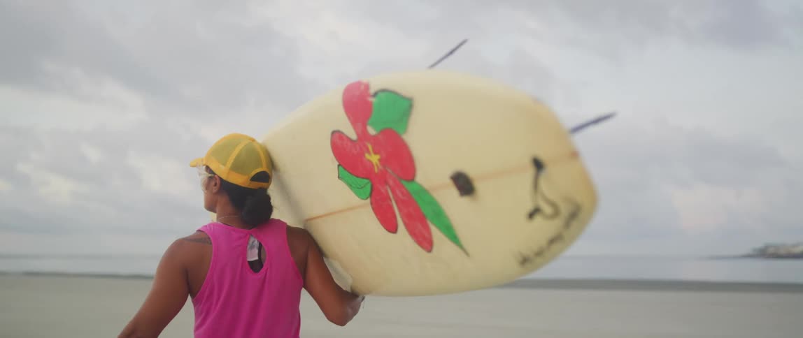 A surfer carries their board with one arm while walking toward the ocean