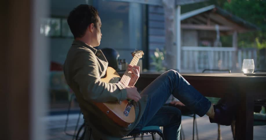 A man is playing the guitar on his porch as a dog walks by