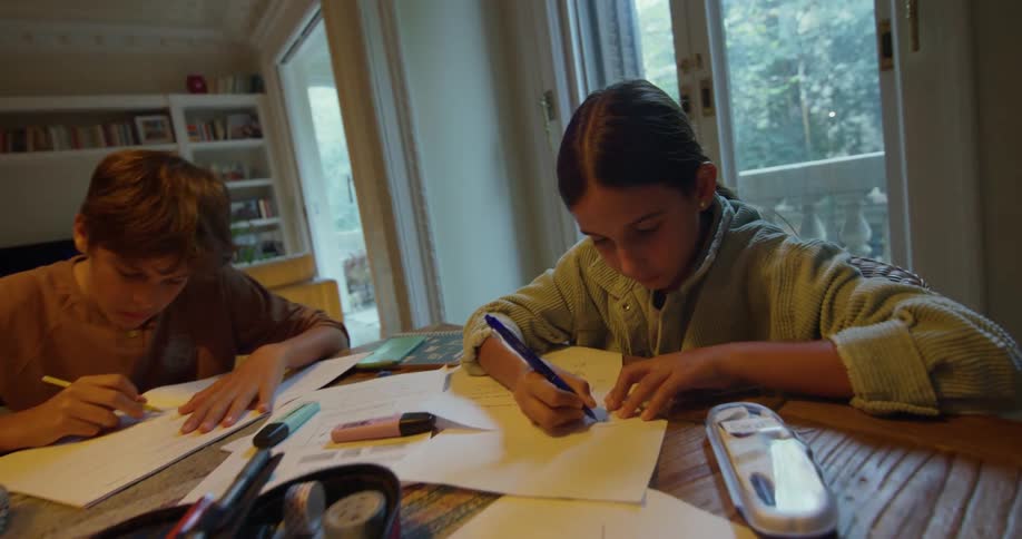 A boy and a girl are drawing at a table in a living room during the daytime