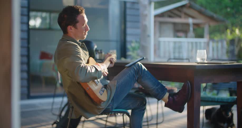 Young man playing guitar sitting on the porch at sunset