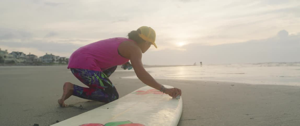 Young man waxing a surfboard over the sand near the beach at sunset