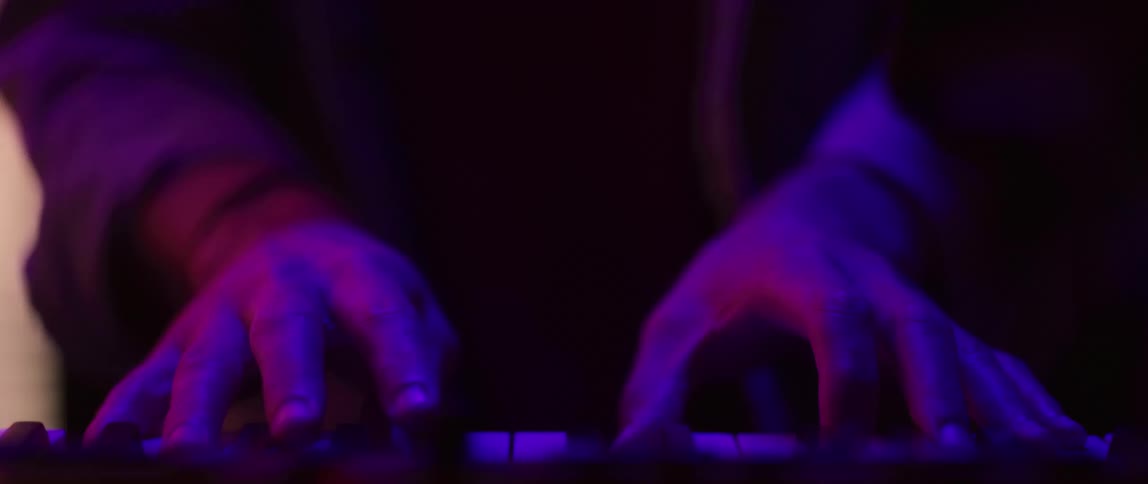 A person is playing on a keyboard piano in a room with flashing lights