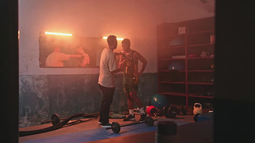 A coach is instructing and encouraging a young athlete in workout room with glowing lights