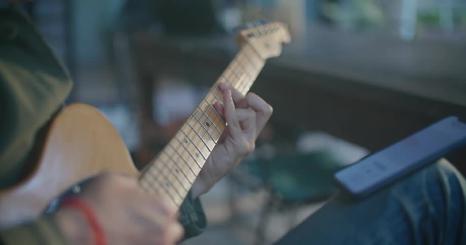 A person touches his phone as he plays the guitar