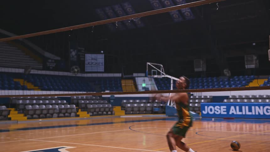 A man practices serving volleyballs in the gym