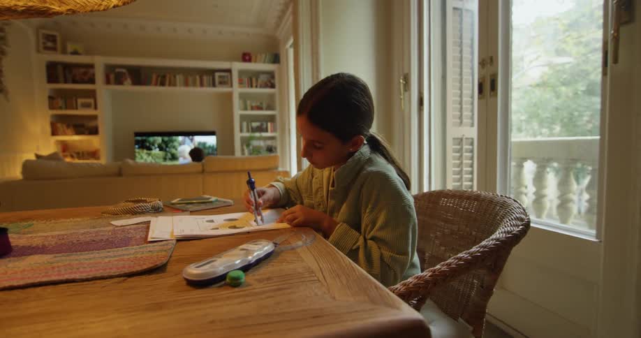 A girl is sitting at a table in the living room while doing a homework assignment during the day