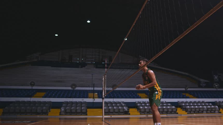 A man hits a ball over a net in a stadium