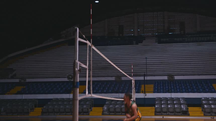 A teenage boy spikes a volleyball over a net in a gymnasium