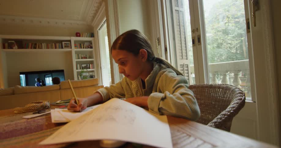 A young girl is sitting at a table in the dining room and drawing on a sketch pad