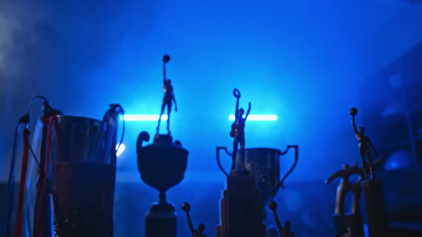 Silhouette of sports trophies lined over a shelf in front of blue lights