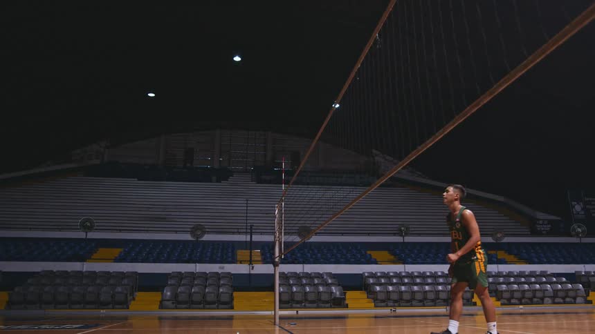 Male volleyball athlete jumps near net to spike the ball in empty stadium