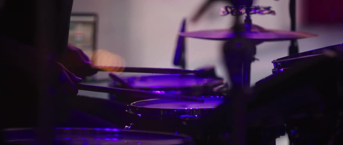 A man plays the drums on stage in front of a large screen and flashing lights