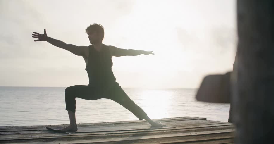 A man does yoga on a wooden pier on the ocean during the day