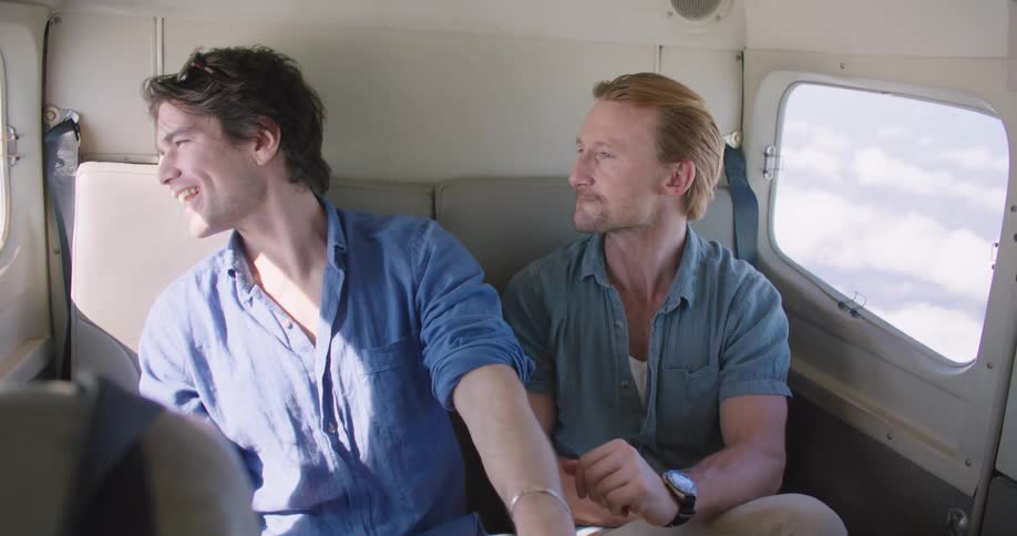 Two men talk and point out the window as they travel in the airplane