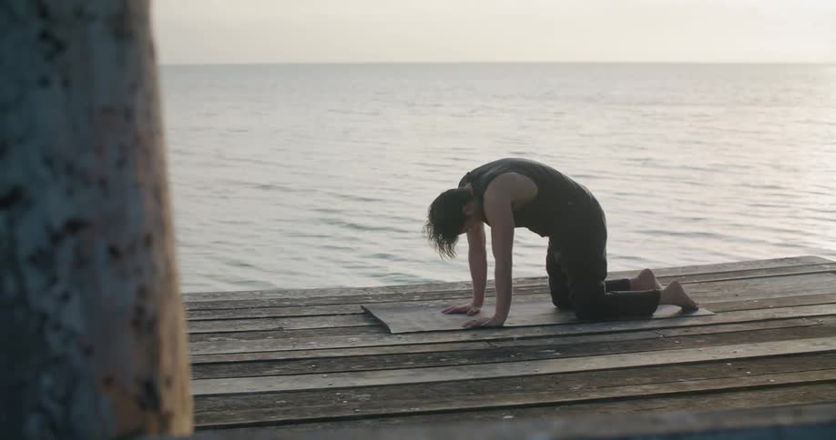 A man does yoga on a wooden dock on the ocean during the day