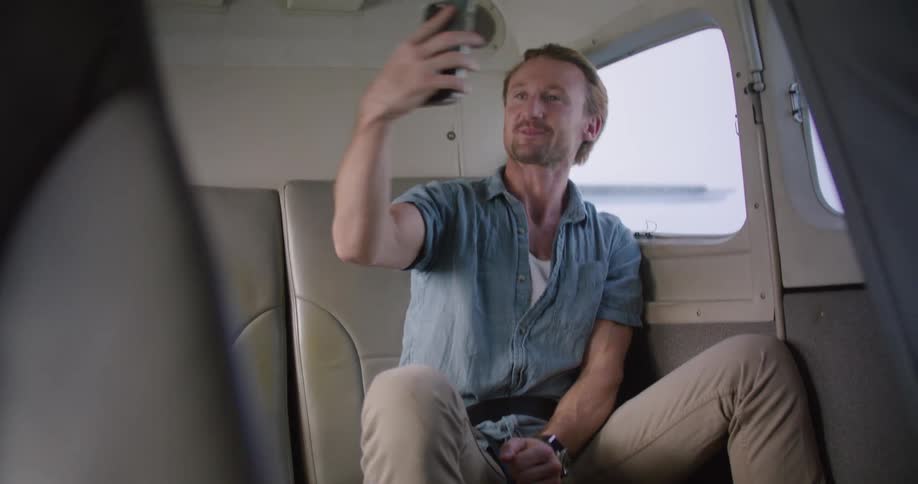 Man wearing seat belt rides in spacious vehicle cabin while making video call and showing the scene outside window via mobile phone