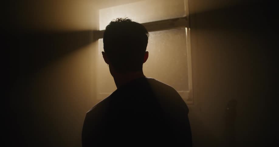 A man in a dark room looking out at a street light