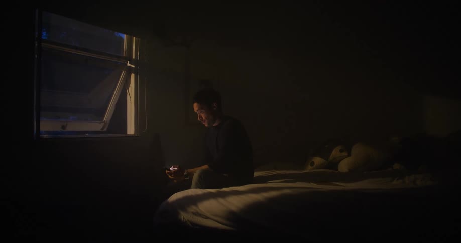 A man uses his smartphone while sitting in a dark bedroom at night