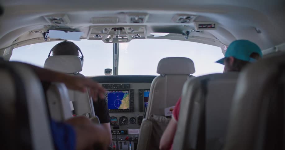 Pilot sits in cockpit with electronic display piloting airplane as two passengers sit in back