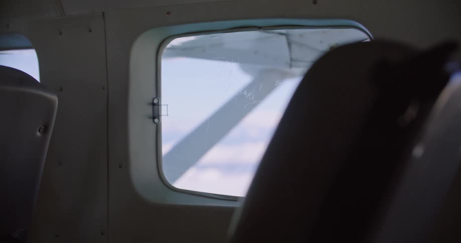 The back of a seat and the window in an airplane looking out at clouds