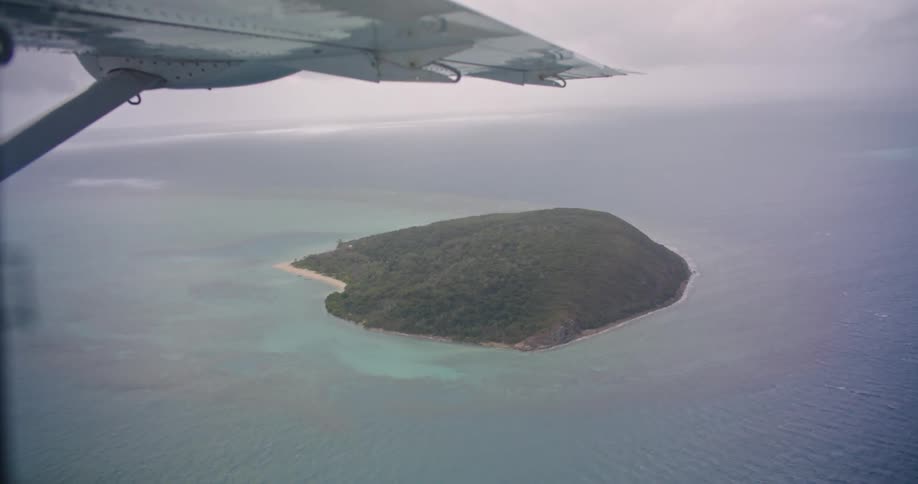The wing of an airplane as it flies past an island in the ocean