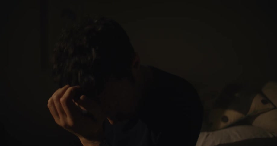 A man sits on the bed rubbing his face