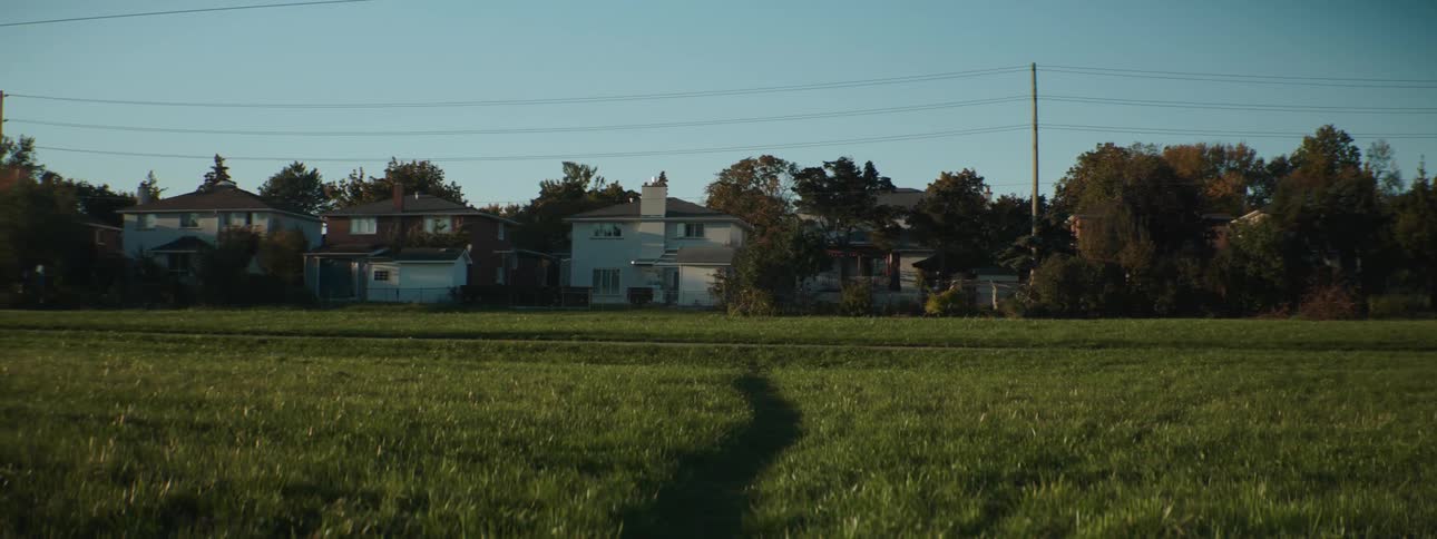 A cyclist rides a bicycle along a path through a field in a residential area during the day