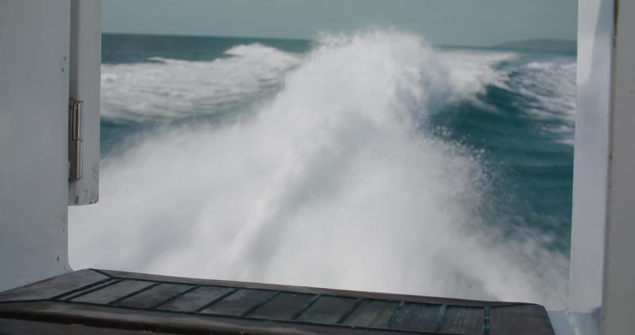 A view from onboard a boat speeding on the ocean violently spraying water and leaving a huge wake on a hazy day
